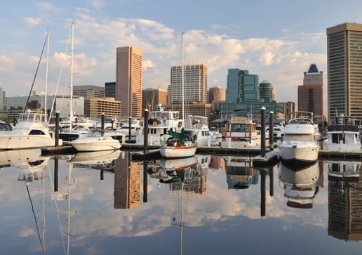 Exterior shot of a city skyline and boats moored at a harbor. 