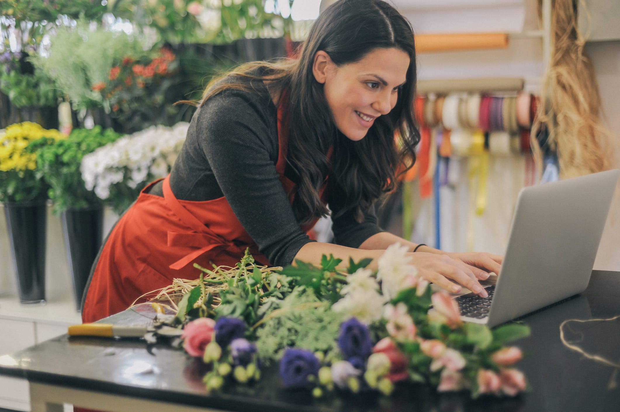A woman uses her laptop while in a florist shop.